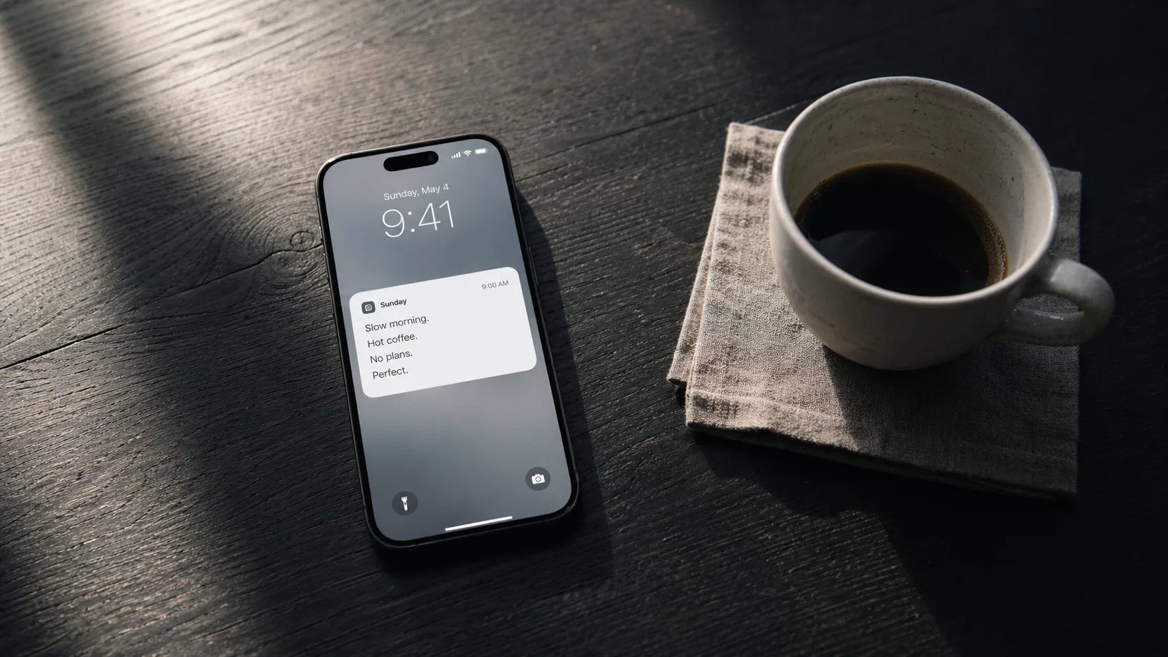 Phone on a dark desk showing a notification card, cup of black coffee beside it